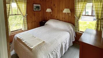 Een slaapkamer met een houten wandpaneel, een bed met een witte dekbedovertrek, twee bedlampjes en een raam met gordijnen.
