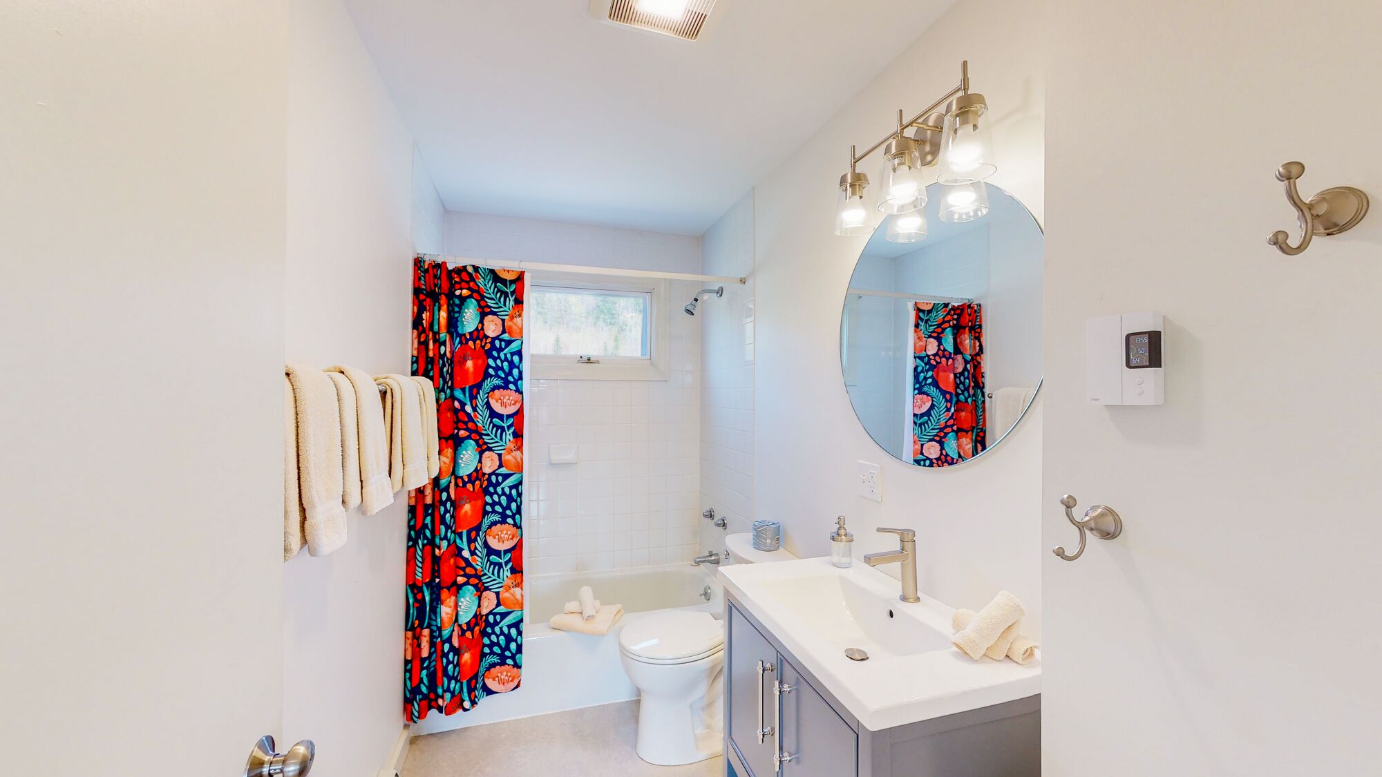 Un baño moderno con inodoro, lavamanos y ducha. Hay un espejo con luces arriba y toallas colgadas en un perchero.