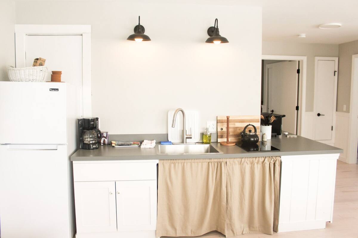 A modern kitchen with a white refrigerator, a coffee maker, a sink, and two pendant lights.