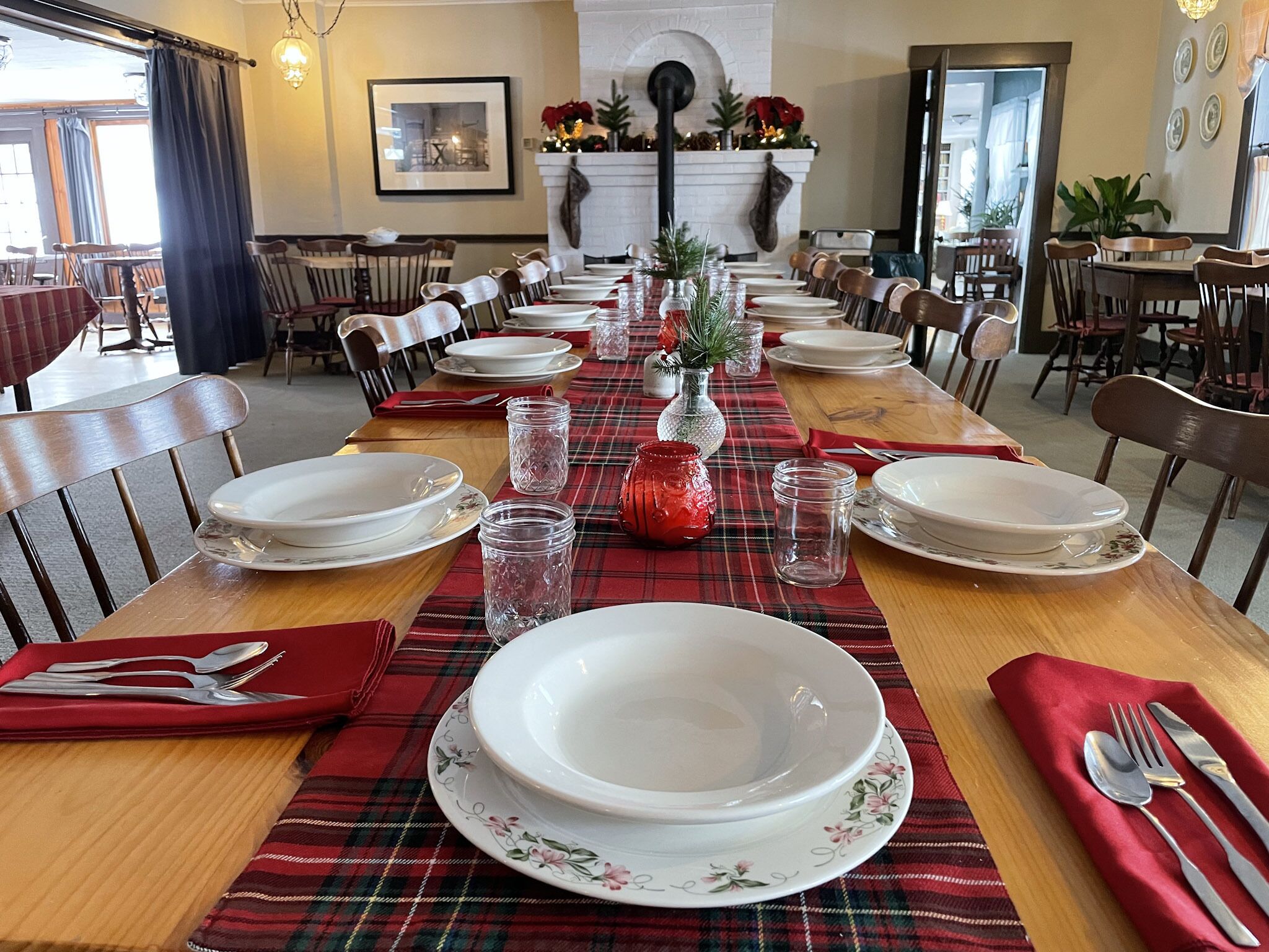 A dining area with a long table set for a meal, featuring plaid tablecloths, white plates, and clear glassware.