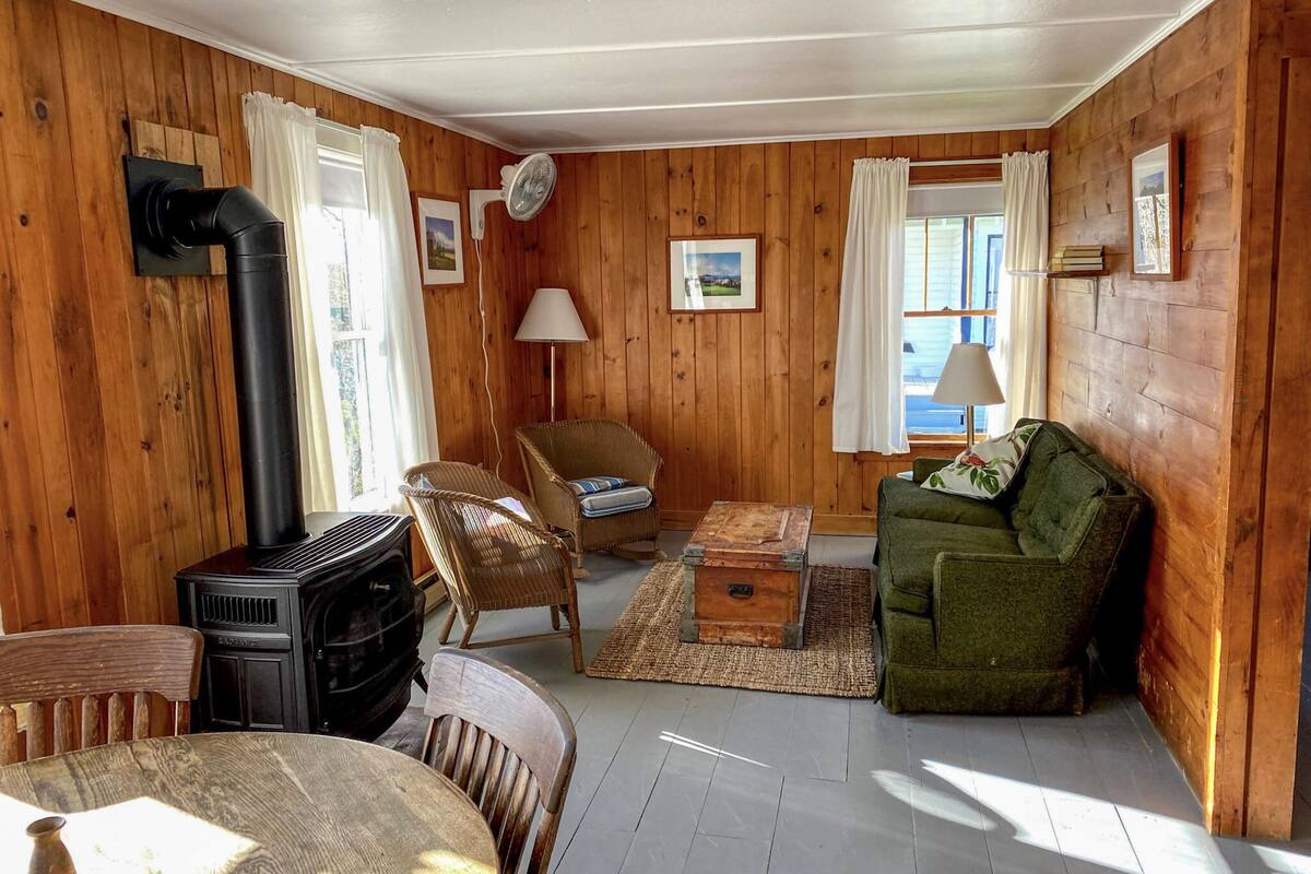 A cozy cabin interior with a wood stove, wicker furniture, and a green sofa.