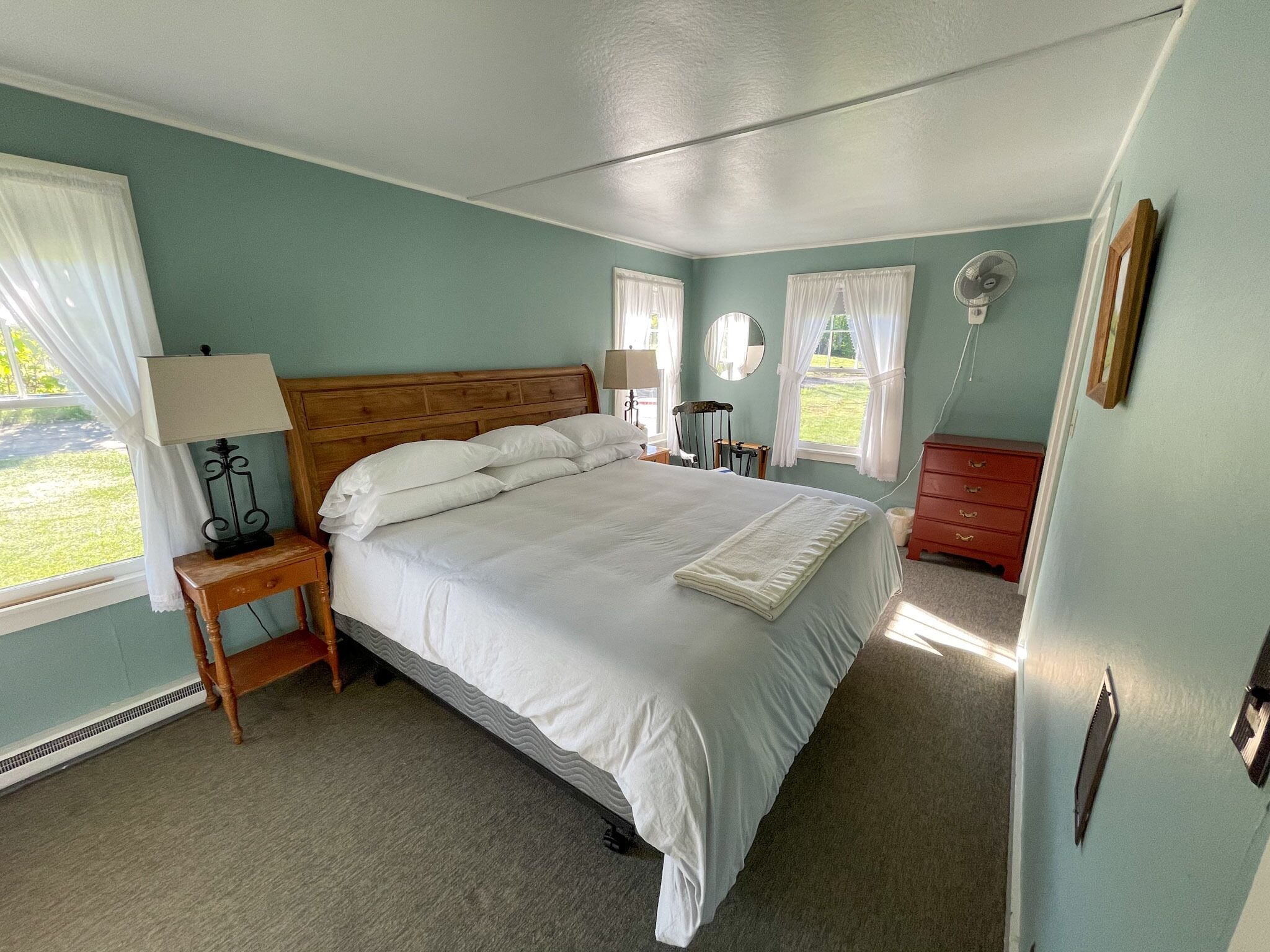 Een net opgemaakt bed in een kamer met lichtblauwe muren, een houten hoofdbord en een klein nachtkastje met een lamp.