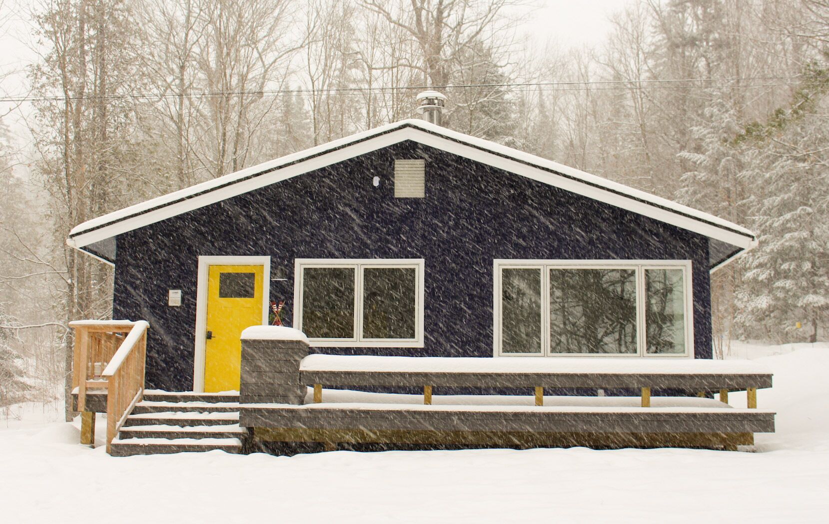 A cabin with a yellow door, large windows, and a covered porch.