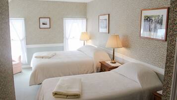 A hotel room with two beds, a nightstand, a lamp, and floral wallpaper.