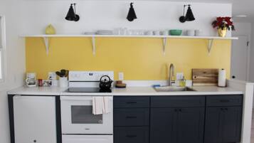A modern kitchen with a white stove, a sink, and dark cabinets. There are hanging lights above the counter and a yellow backsplash.