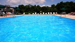 A swimming pool with clear blue water, surrounded by lounge chairs and umbrellas. - American Heritage RV Park (Williamsburg)