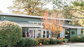 A building with a green exterior, a covered porch, and a small front yard with a tree and potted plants. - American Heritage RV Park (Williamsburg)