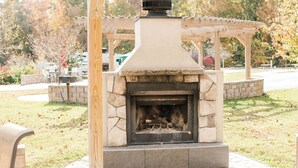 A stone fireplace with a chimney, surrounded by a wooden pergola and a stone wall. - American Heritage RV Park (Williamsburg)