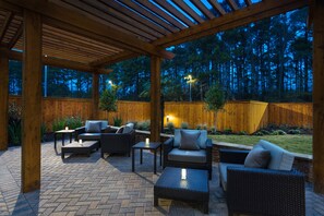 An outdoor patio area with wooden pergola, wicker furniture, and a view of a wooded area.