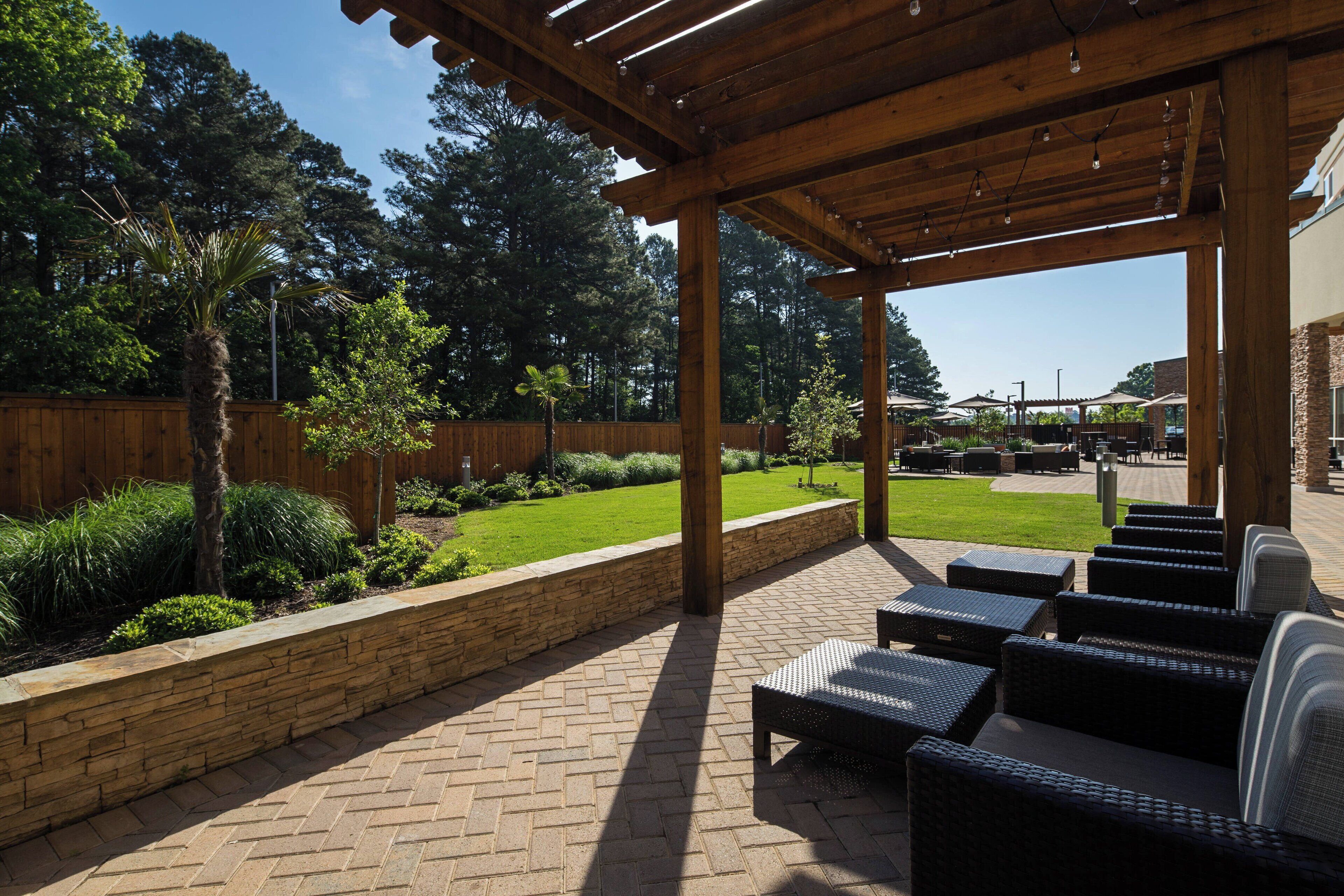 An outdoor patio area with wicker furniture, a stone retaining wall, and a wooden pergola.