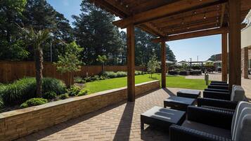 An outdoor patio area with wicker furniture, a stone retaining wall, and a wooden pergola.