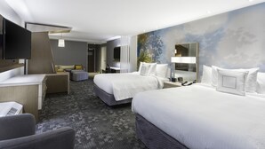 A hotel room with two beds, a desk, a chair, a TV, and a bathroom.
