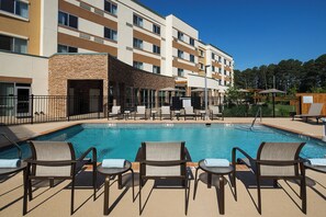 A hotel pool area with lounge chairs and umbrellas, surrounded by a fence.