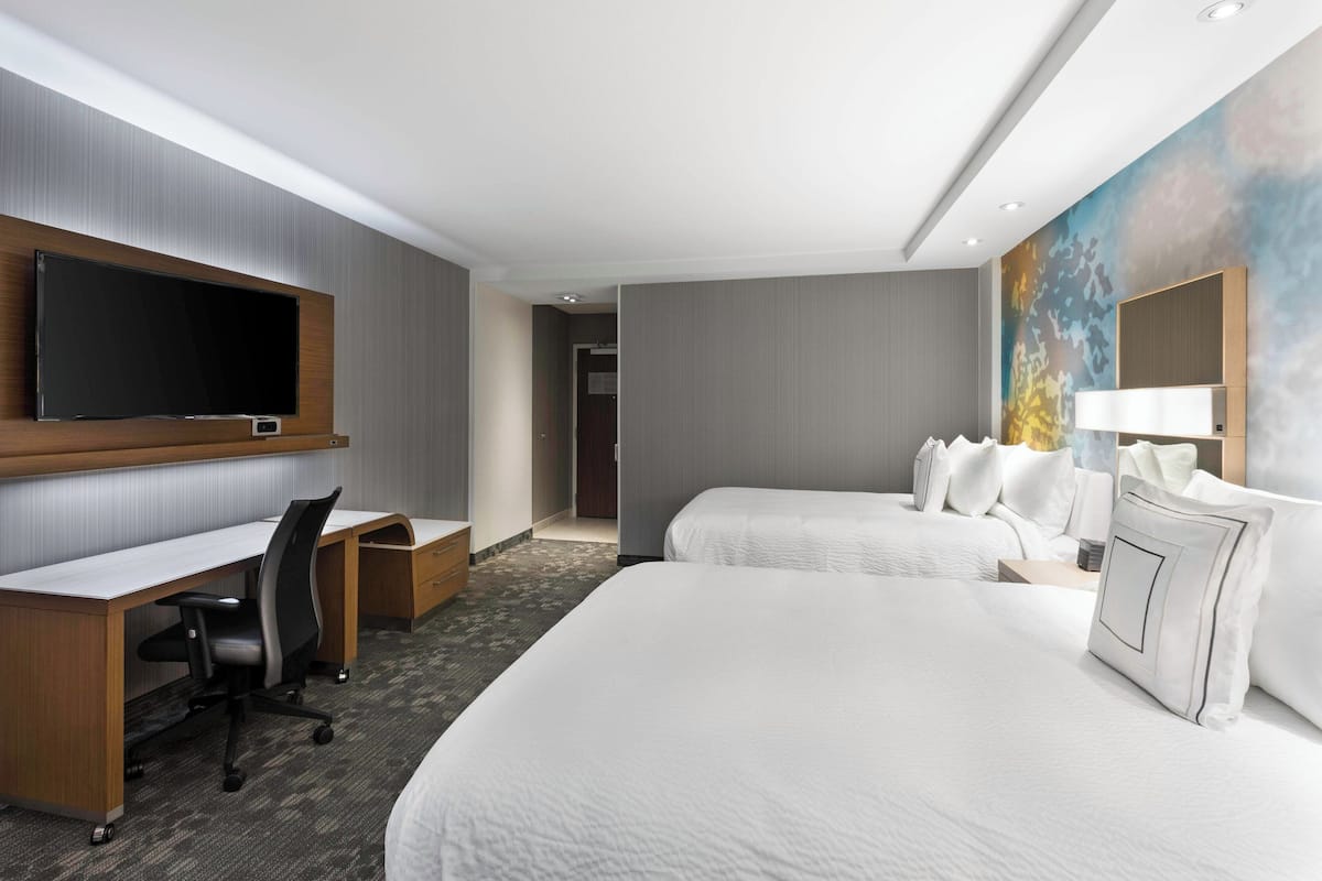 Habitación de hotel con dos camas, un escritorio, una silla, un televisor de pantalla plana y un ventanal grande.