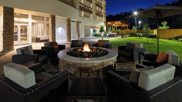 An outdoor patio area with a stone fire pit surrounded by wicker furniture and a covered seating area.
