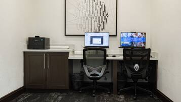 A small office with two desks, one with a computer and a monitor, and a chair in front of it.
