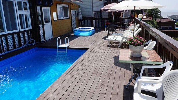 Ett trädäck med en pool, solstolar och ett bord med ett parasoll.