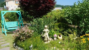 En trädgård med en turkosfärgad gunga, en staty och diverse växter och blommor.
