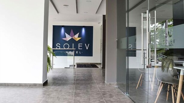 A modern hotel lobby with a large sign reading "SOLEV HOTEL" and a glass wall with a dining area visible.