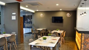 A modern dining area with multiple tables and chairs, a flat-screen TV mounted on the wall, and a unique illuminated countertop.