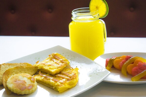 Un plato de desayuno con tostadas, una tortilla y fruta, además de un vaso de jugo de naranja.