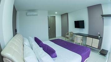 Una habitación de hotel con cama, escritorio, silla, televisión y una mesita.
