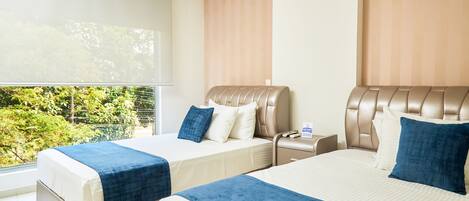 A hotel room with two beds, a large window, and a view of greenery outside.