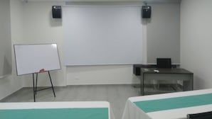 A conference room with a whiteboard, a projector screen, a table, and two beds with green bedspreads.