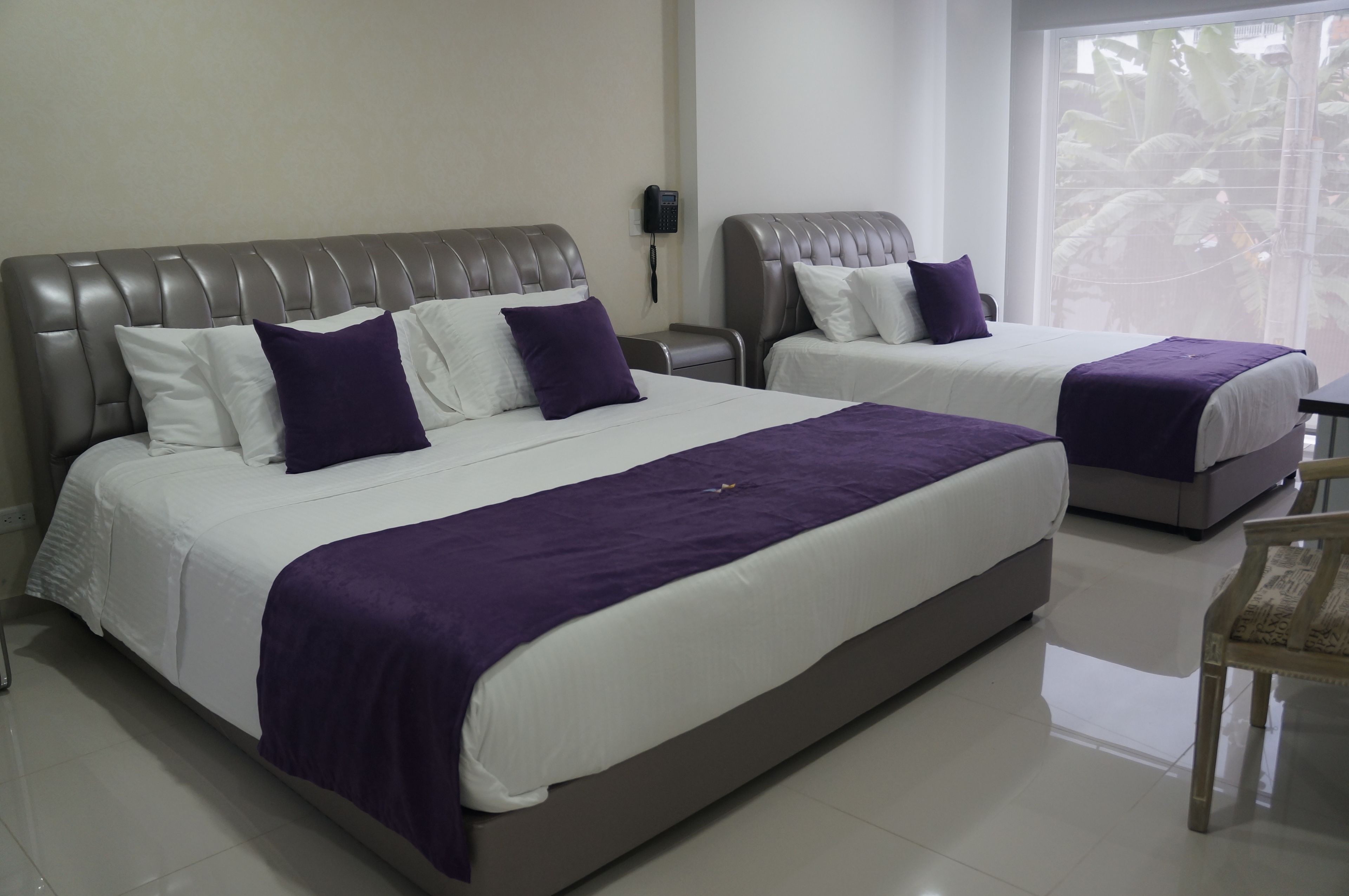 A hotel room with two beds, each with a headboard, white bedding, and purple accents.