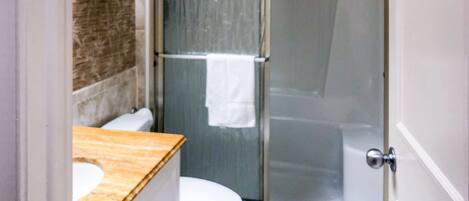 Een badkamer met een houten wastafelmeubel, een wit toilet en een douchecabine met glazen wanden.