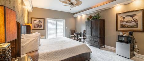 A bedroom with a large bed, a ceiling fan, a small kitchenette, and a dining area.