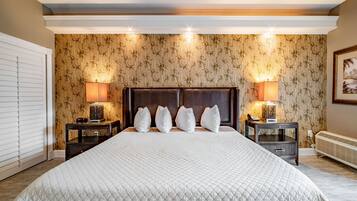 Uma cama grande com edredom branco acolchoado, duas mesas de cabeceira com abajures, e uma parede com papel de parede de bambu.