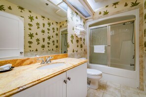 Un baño con lavamanos de mármol, inodoro blanco y ducha con cerramiento de vidrio.