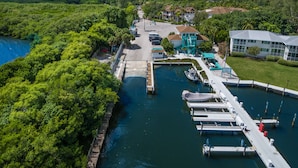 Vue aérienne d’une marina avec des bateaux amarrés, une promenade et une végétation luxuriante environnante.
