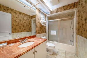 A bathroom with a marble sink, a toilet, a glass-enclosed shower, and bamboo-patterned walls.