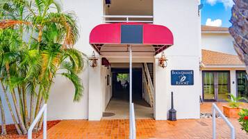 A building entrance with a red awning, a sign reading "Boca Grande Resort," and a staircase leading to an upper level.