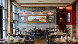 A restaurant with wooden tables and chairs, framed pictures on the wall, and a brick wall. - Great Wolf Lodge Colorado Springs (Colorado Springs)