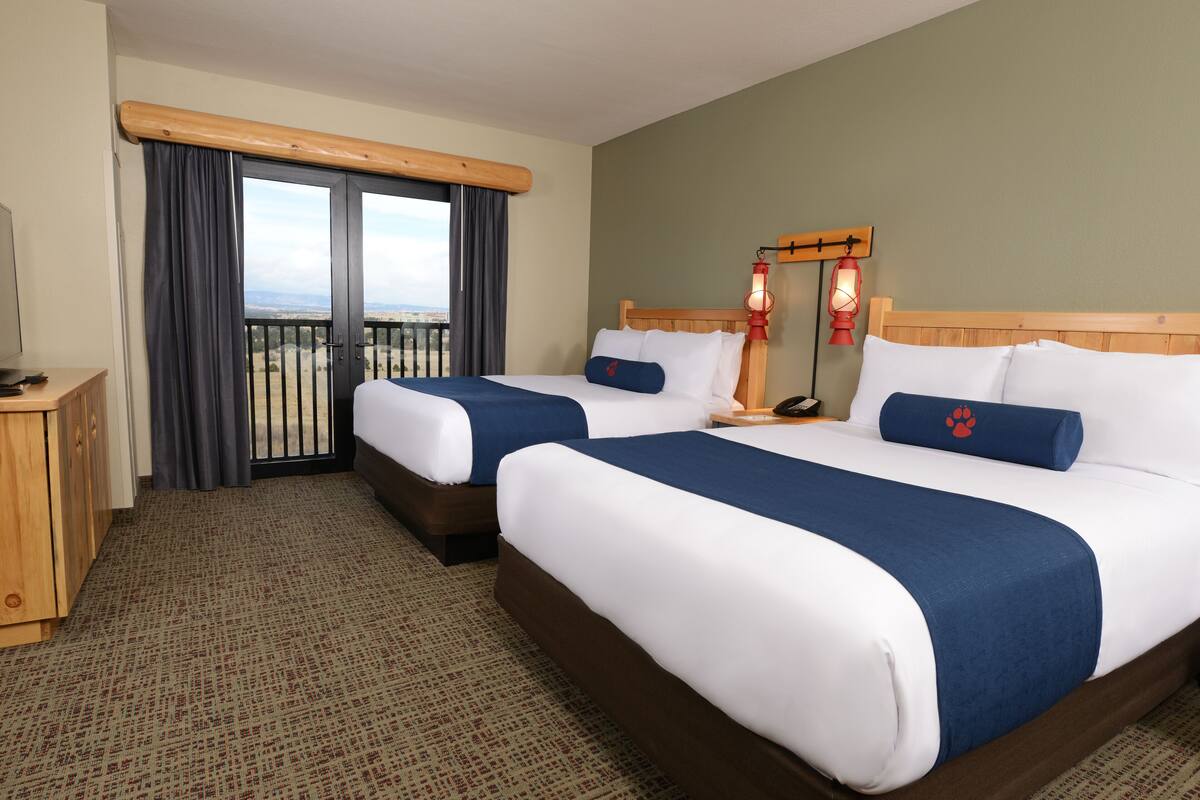 A hotel room with two beds, a balcony, a wooden headboard, and a view of the city.