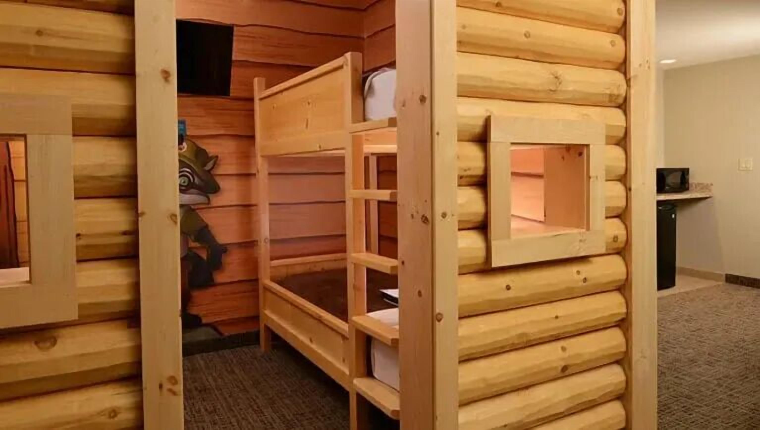 A log cabin-style room with bunk beds, a small window, and a desk with a computer.