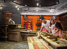 Un interior rústico con mesas de madera, un barril y una pared que exhibe objetos coloridos.