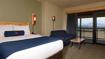 A hotel room with a bed, a sofa, a small table, a nightstand, and a balcony with a view.