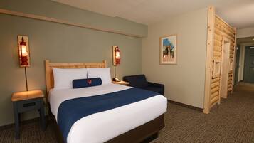 A hotel room with a large bed, two bedside tables with lamps, a chair, a wooden wall panel, and a painting on the wall.