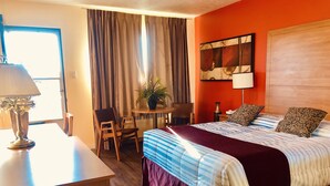 A hotel room with a bed, a desk, a chair, a table with a plant, and a window with curtains. - Martin's Inn (Cornwall)