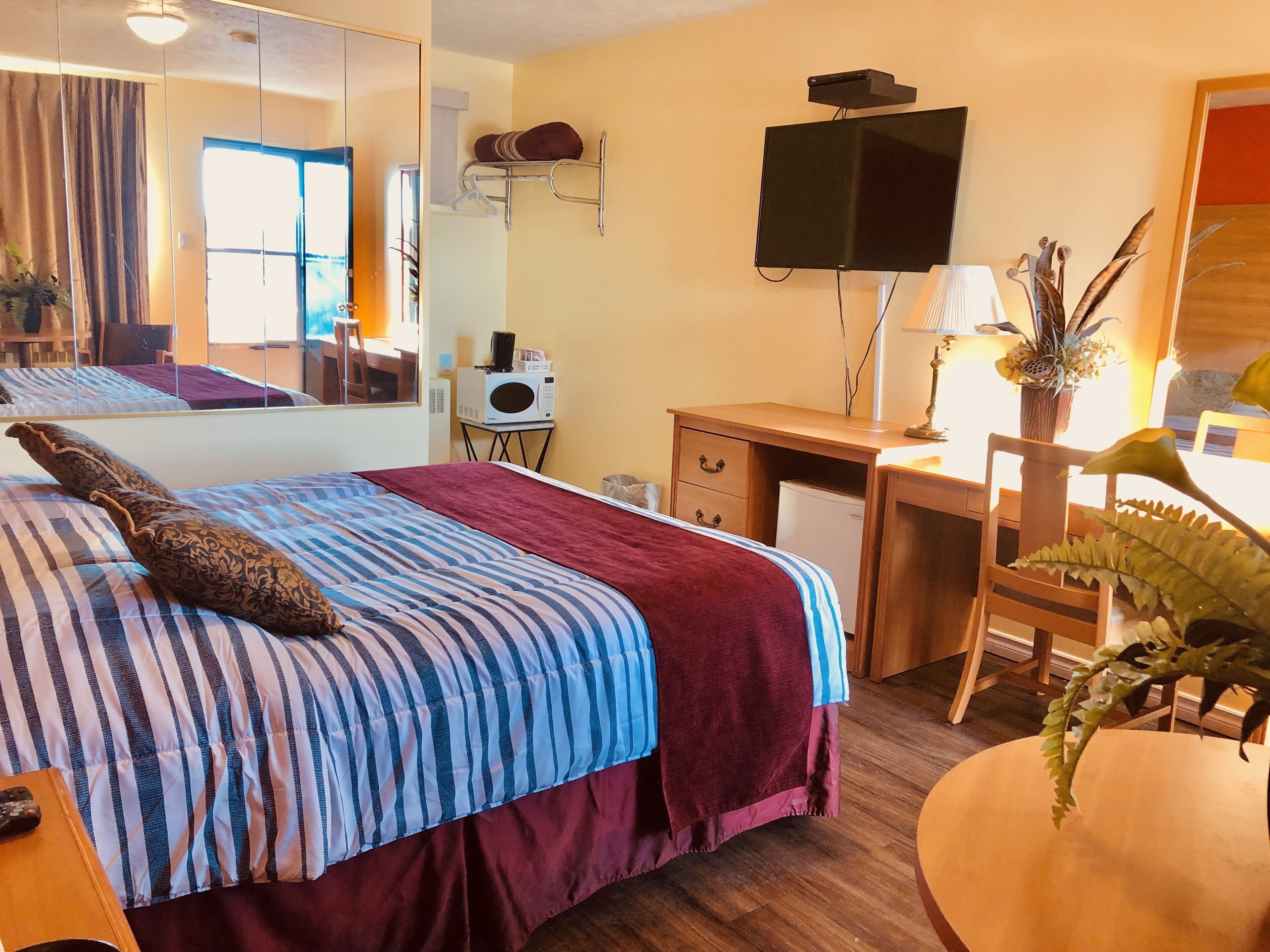 Ein Schlafzimmer mit Bett, Schreibtisch, Stuhl, Fernseher, Mikrowelle und Spiegel.