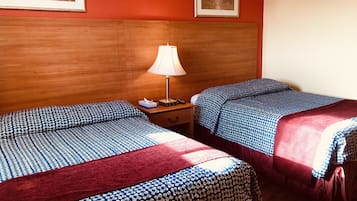 Quarto de hotel com duas camas, cabeceira de madeira, mesa de cabeceira com abajur e quadros nas paredes.