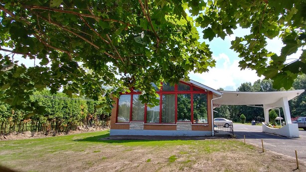A small, modern building with a red and white exterior, a covered entrance, and a parking area with a few vehicles. - Martin's Inn (Cornwall)