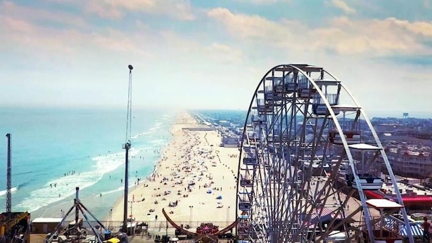 Ein Strand mit einem großen Riesenrad und einer Pier, die sich ins Meer erstreckt.