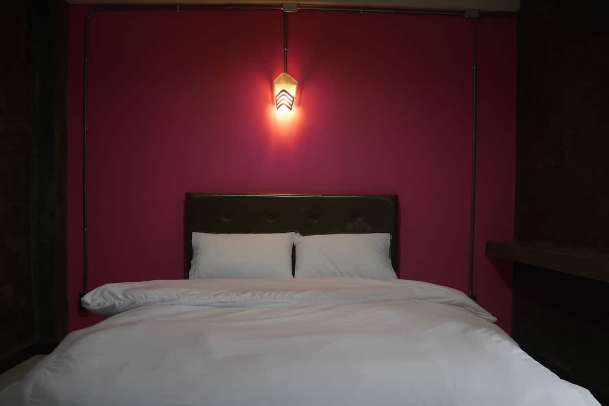 A bed with white bedding in a room with red walls and a dark headboard.