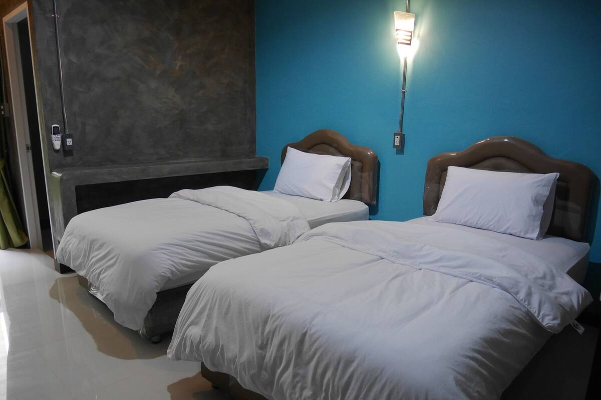 A hotel room with two beds, a blue wall, and a modern light fixture.