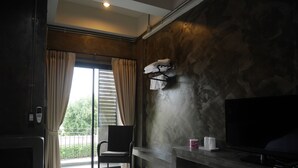 A hotel room with a bed, a TV, a small fridge, a chair, and a window with curtains. - Green Garden Place (Udon Thani)